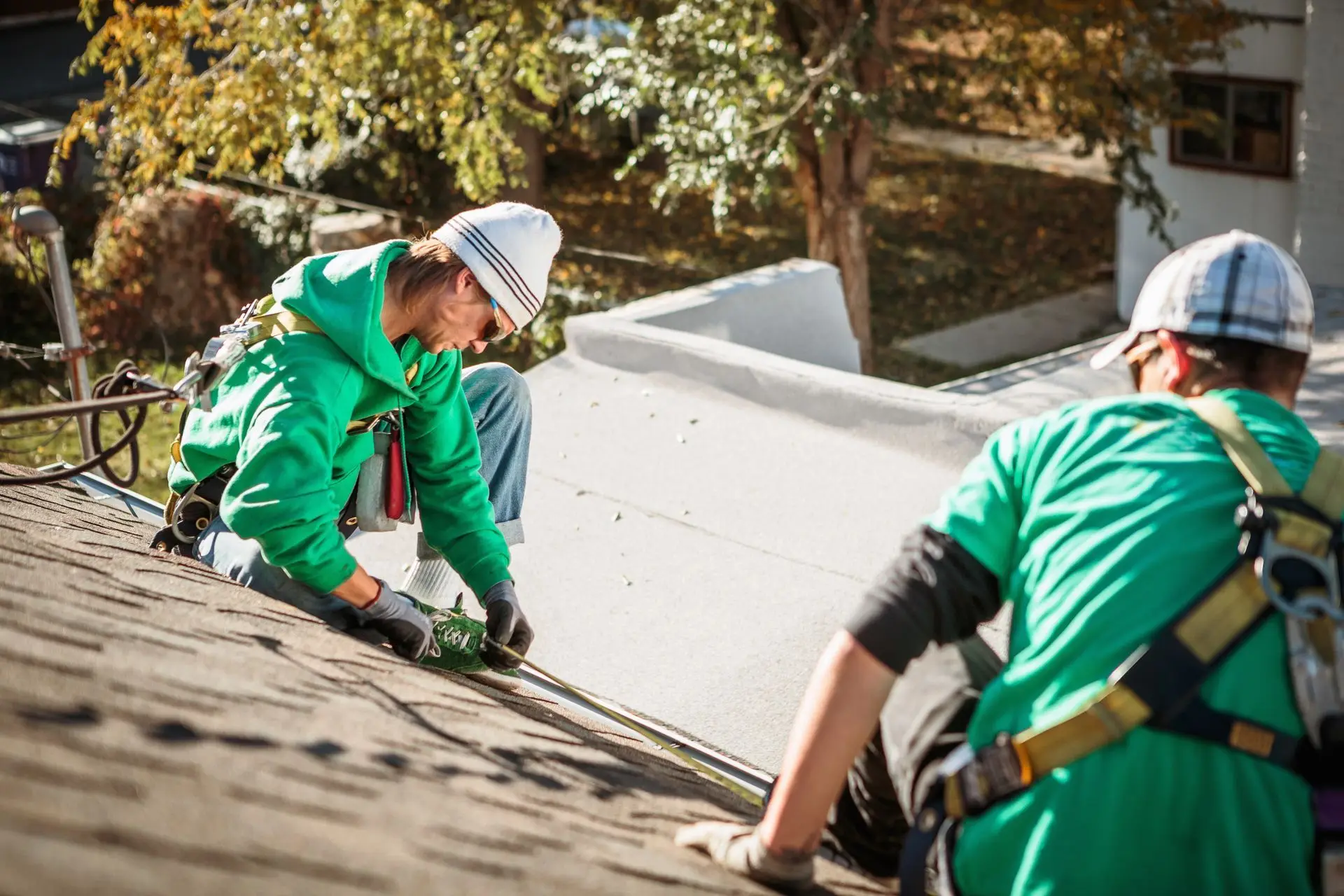 Two workers on a rooftop installing a black cable, wearing safety harnesses and green shirts.